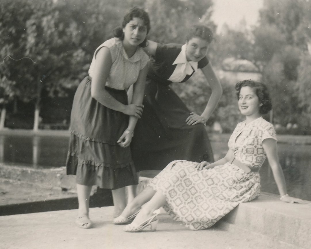 Three women posing by a pond in a vintage black and white photograph, showcasing 1940s fashion.